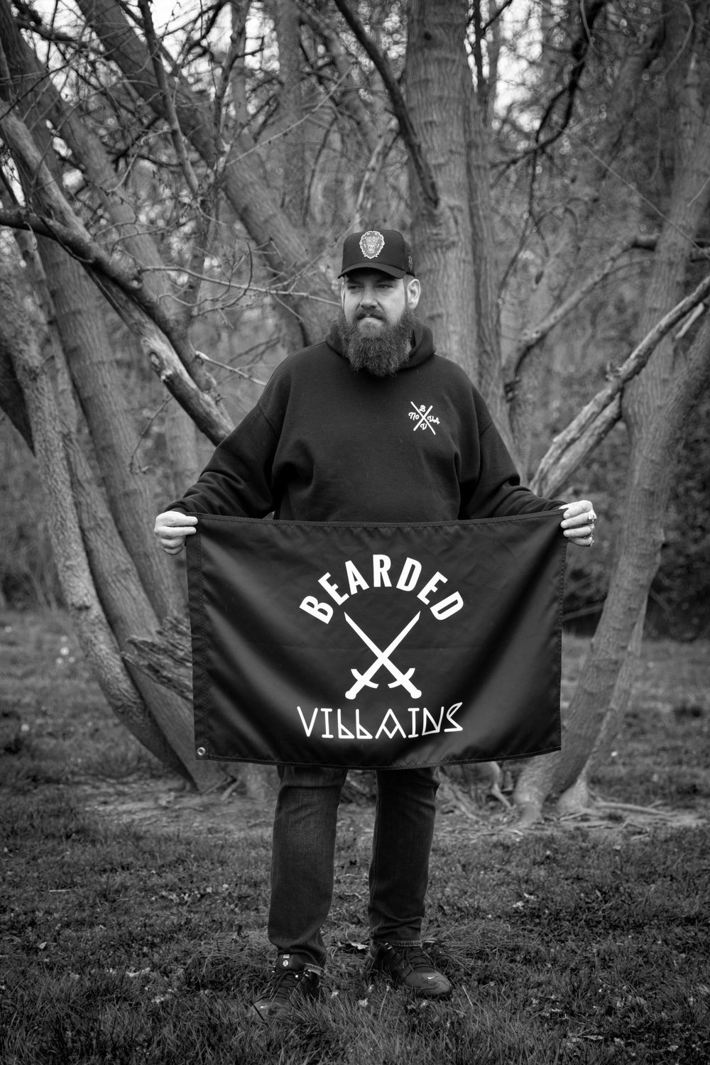Person displaying a black flag with crossed swords emblem in a wooded setting.