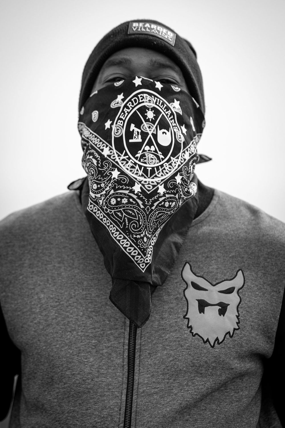 Person wearing a bandana mask with intricate tribal designs and a baseball cap in black and white.