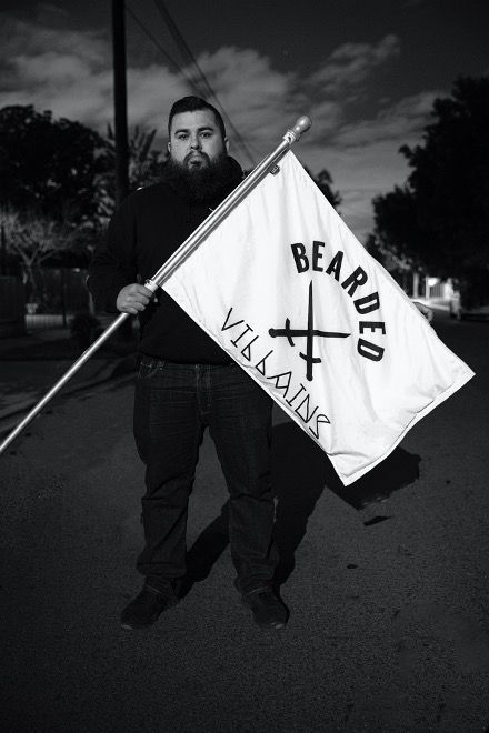 Figure holding a white flag with crossed swords and 'BEARDED' text in black and white photography.