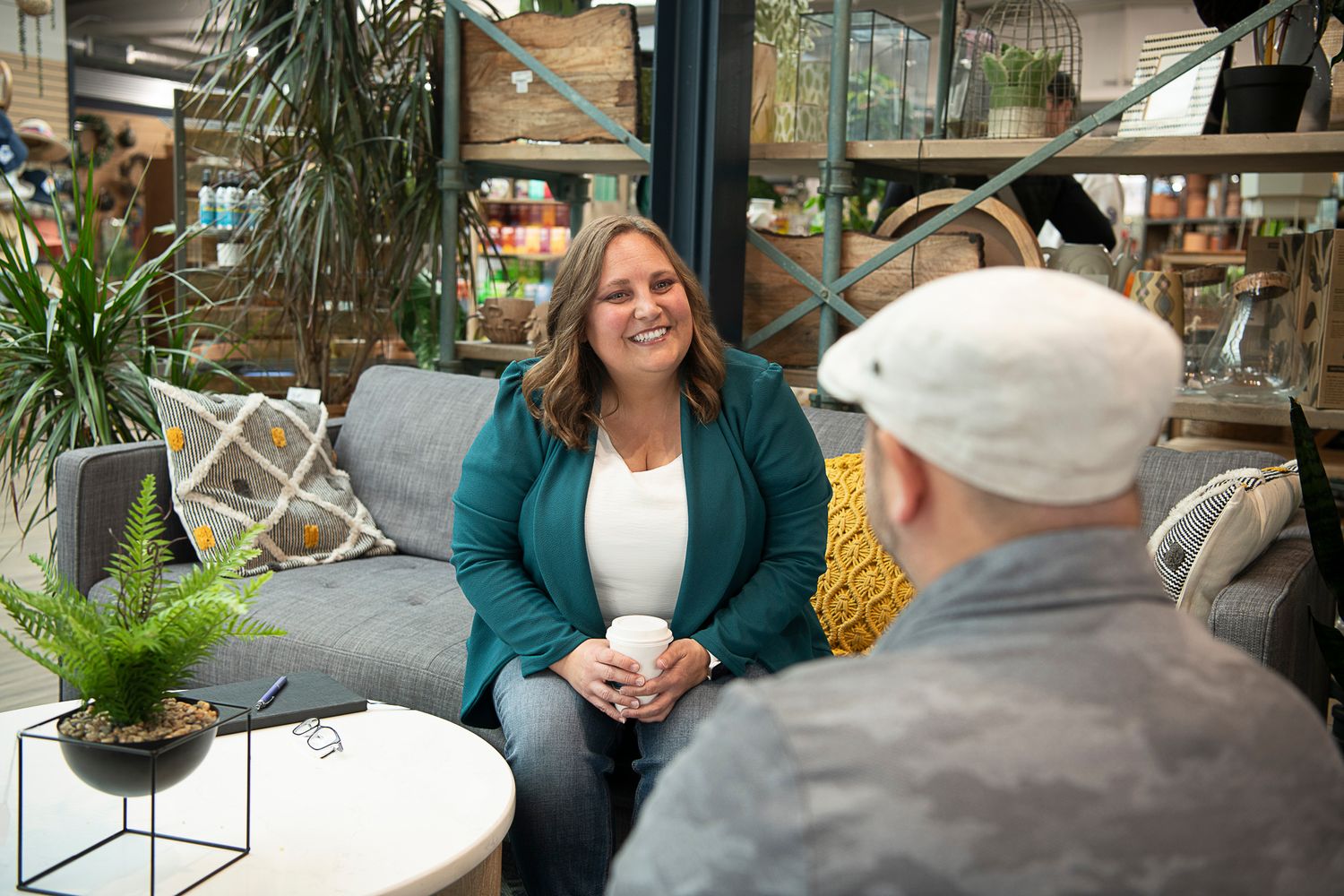 A casual cafe conversation over coffee with cozy seating and plants decorating the space.