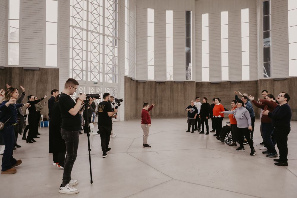 Photographers lined up along walls of large indoor space taking pictures of subject in center of room.