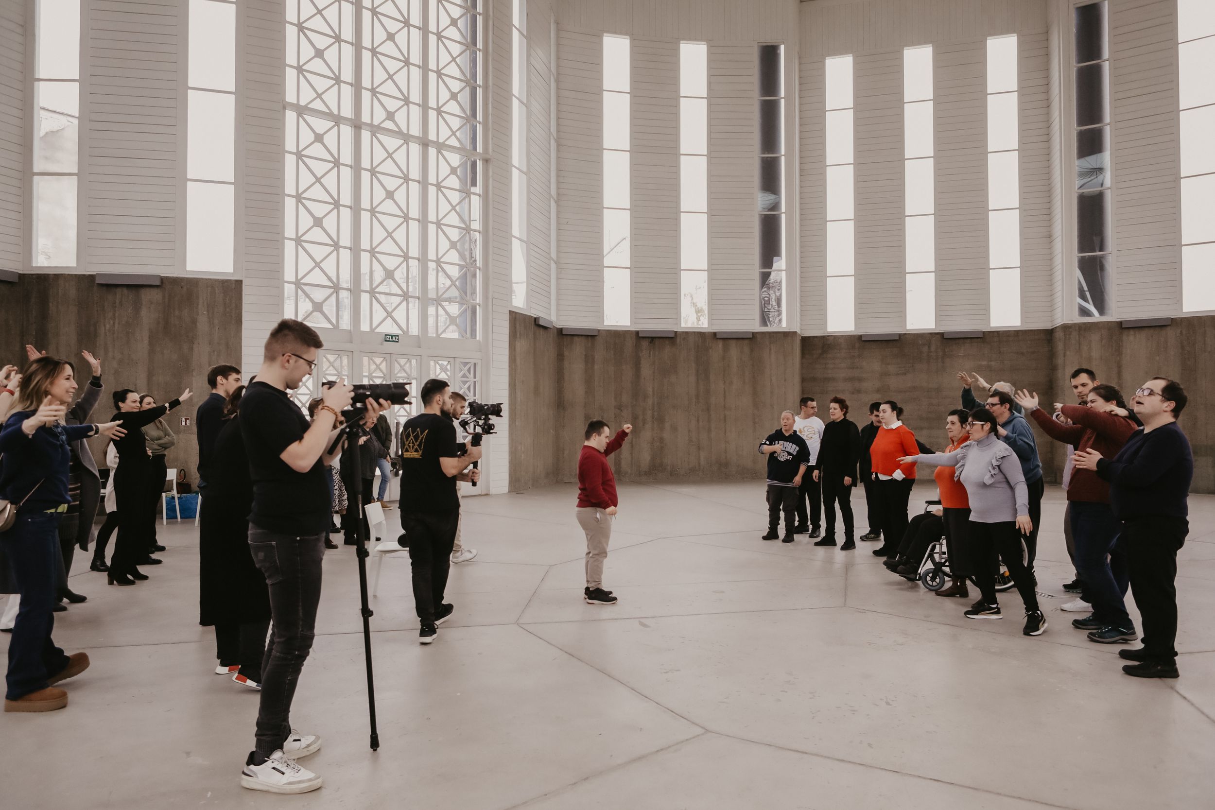 Photographers lined up along walls of large indoor space taking pictures of subject in center of room.