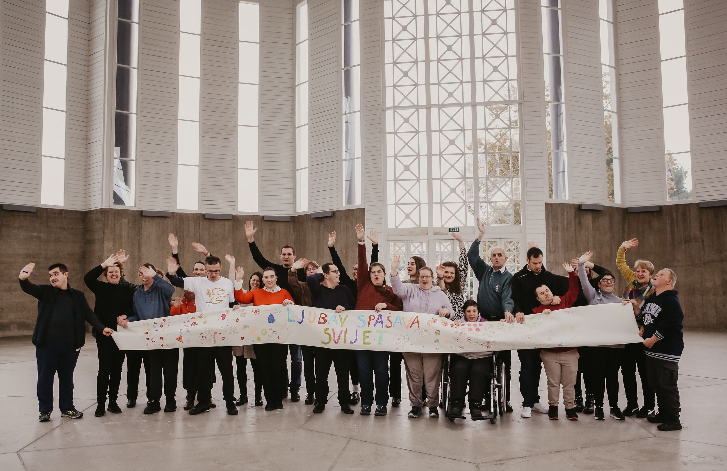 Large group of people posing together in modern architectural space with tall windows.
