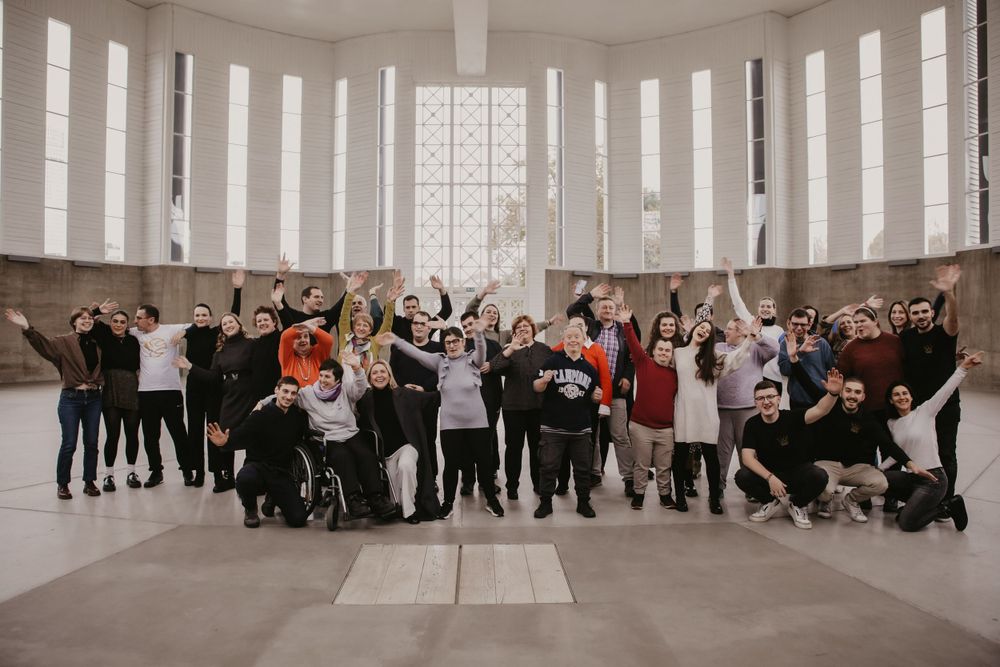 Large group of people posing together in a bright circular room with windows.