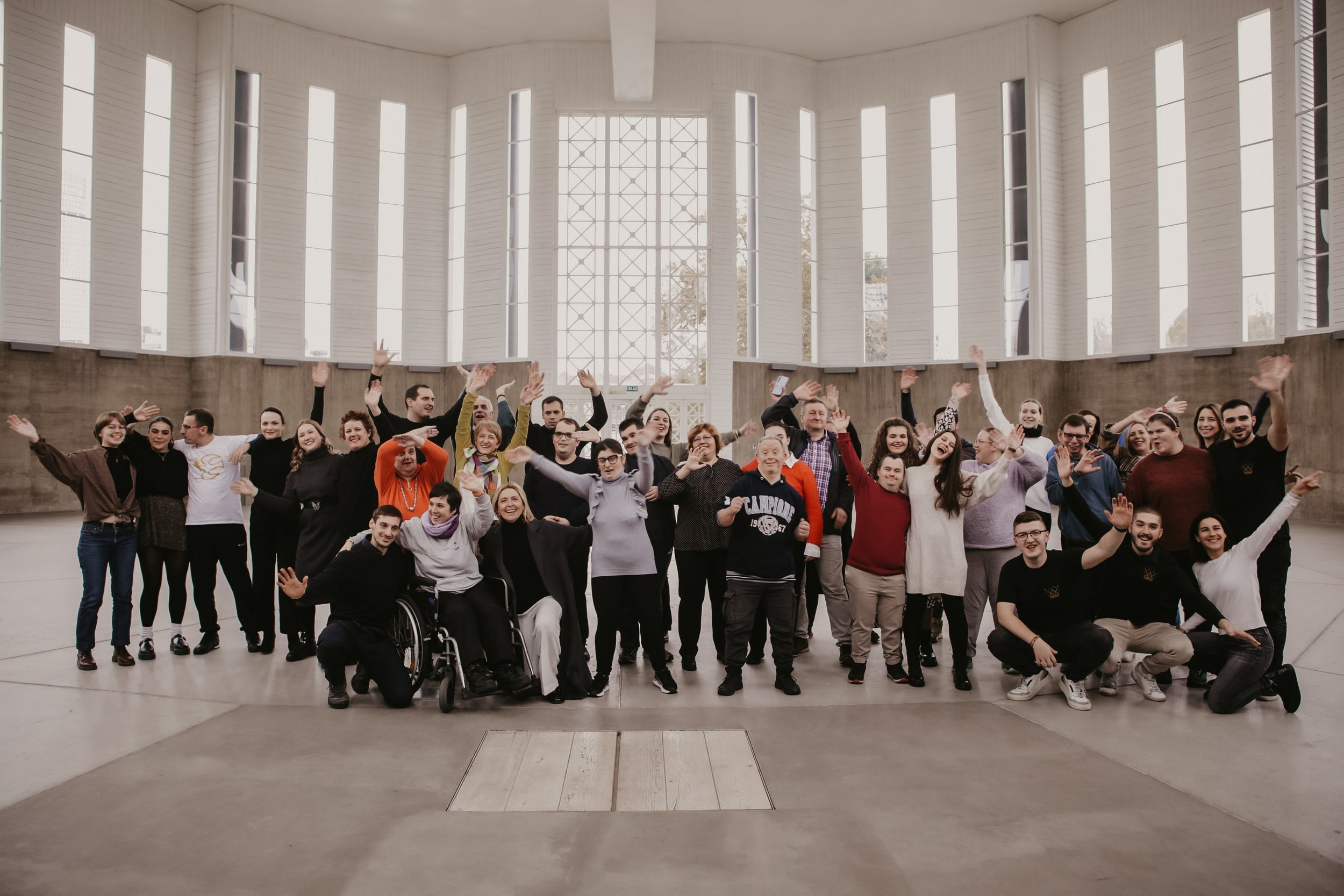 Large group of people posing together in a bright circular room with windows.