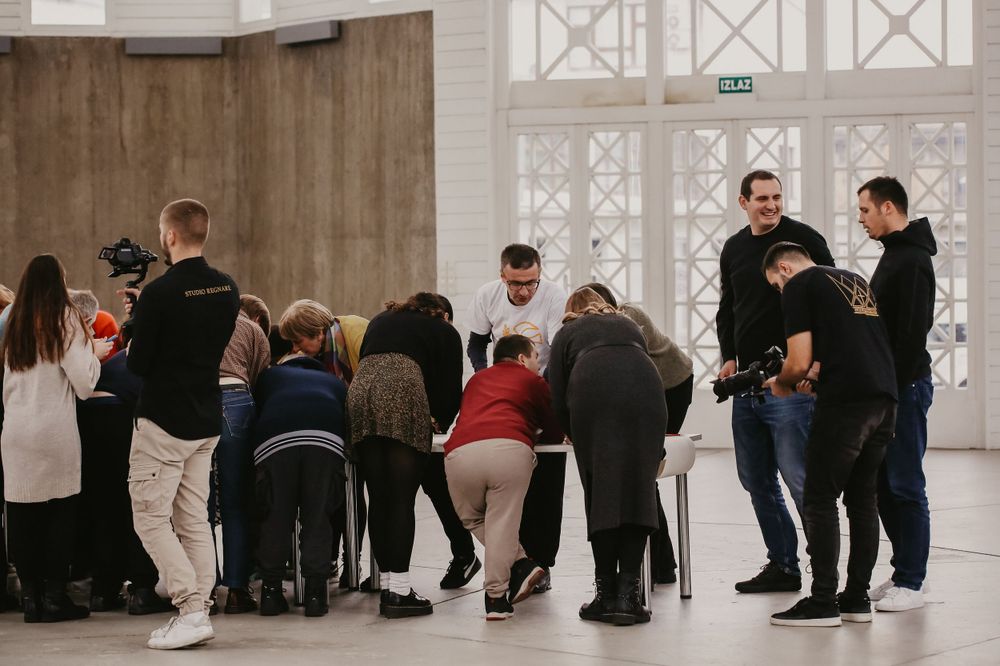 A crowd gathers in discussion inside a modern building with architectural windows.