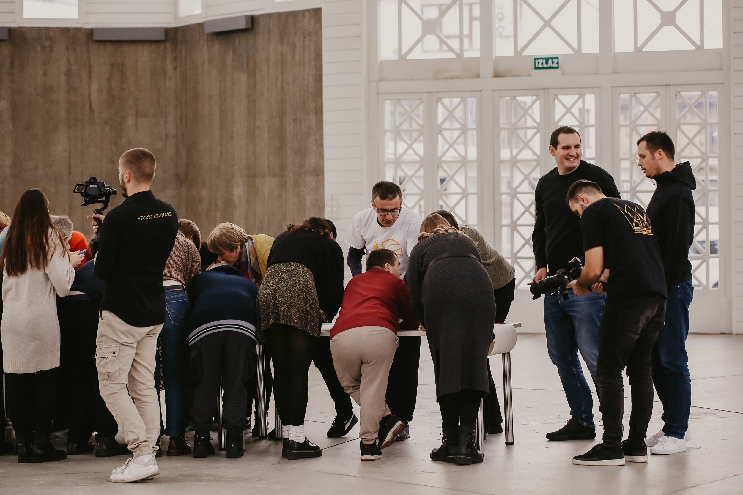 A crowd gathers in discussion inside a modern building with architectural windows.