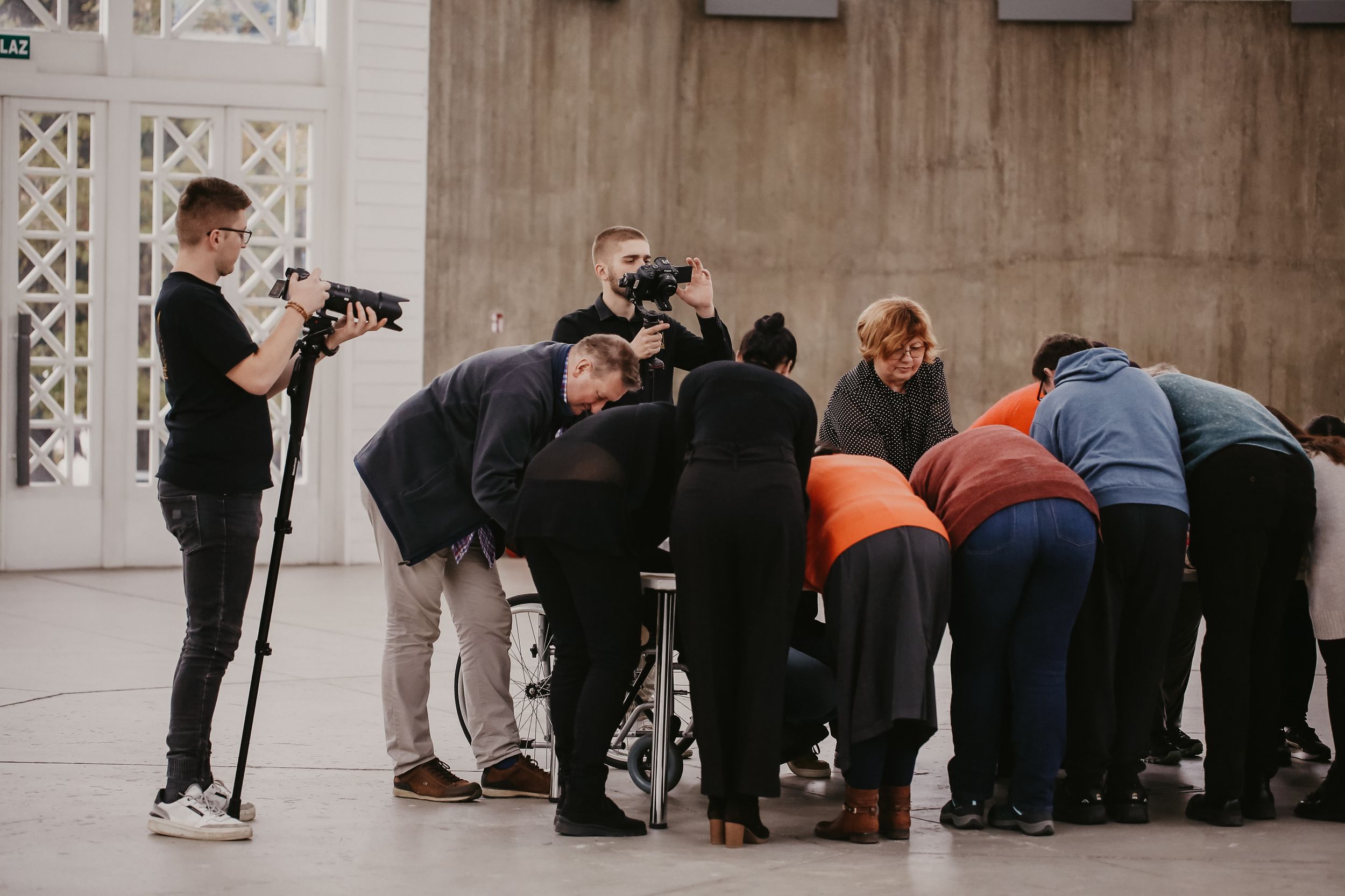 Photographers and a group huddle together during a photo session in an indoor space.