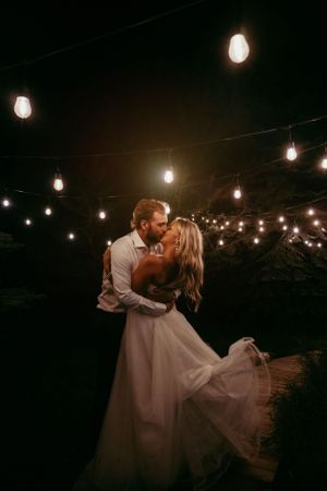 Romantic evening dance under string lights with couple in wedding attire.