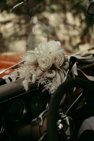 Elegant white roses and dried floral bouquet resting on dark surface in moody lighting with bokeh background.