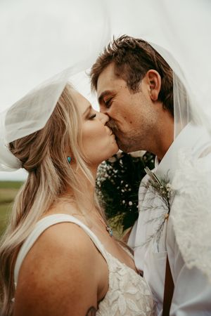 Romantic wedding portrait of a couple sharing an intimate kiss under a flowing veil outdoors.