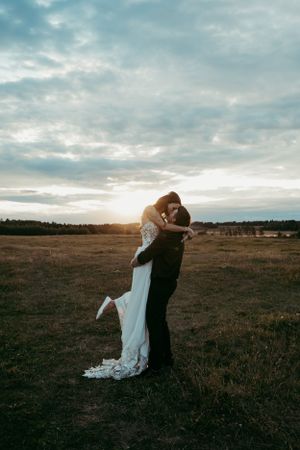 Sunset wedding portrait in an open field with dramatic cloudy sky backdrop.