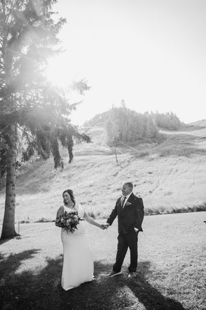 Black and white photo of bride and groom holding hands in scenic outdoor wedding setting with trees and rolling hills.