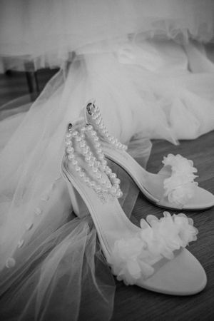 White bridal shoes with pearl embellishments and floral details displayed with flowing tulle veil.