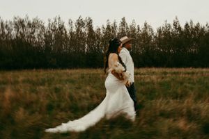 Couple embracing in wedding attire during sunset in rustic field setting.