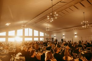 A grand reception hall filled with wedding guests during golden hour with elegant chandeliers overhead.