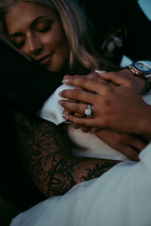 Close-up of hands showing engagement ring and intricate tattoo artwork on arm.