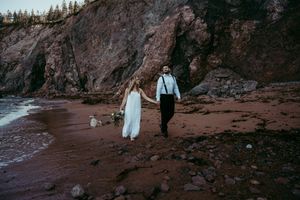 Couple walking along dramatic rocky beach coastline in formal attire.