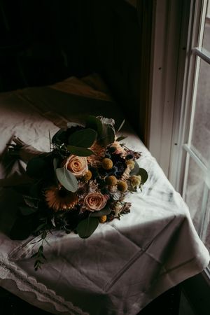 Moody floral arrangements with roses and sunflowers sit on windowsills casting dramatic shadows on white linens.