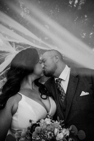 A romantic black and white wedding photo of a couple kissing while the bride holds a floral bouquet.