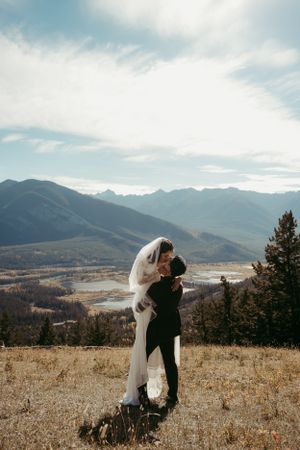 Couple embraces on a mountainside overlooking a scenic valley landscape.