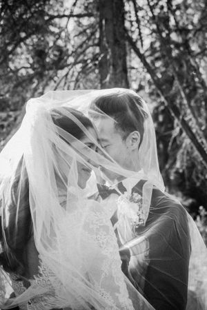 Artistic black and white wedding portrait with veil flowing between couple during intimate moment.