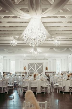 Elegant wedding reception venue with crystal chandeliers, white decor and round tables set for a formal celebration.