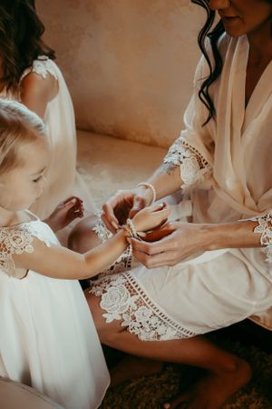 Intimate moment between bride and flower girl in matching white lace robes during wedding preparations.