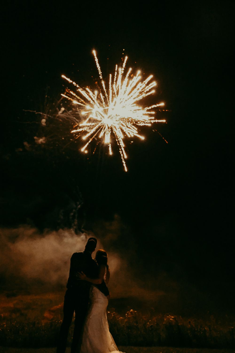 A burst of fireworks illuminates a couple's silhouette against the night sky.