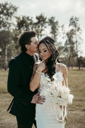 Romantic wedding portrait of couple in natural outdoor setting with bride holding white bouquet.
