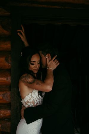 Wedding photography of bride in white lace dress posing dramatically against dark wooden wall.