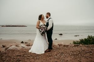Wedding couple standing on rocky beach shore with ocean backdrop.