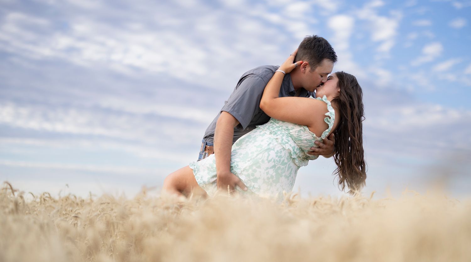 Romantic couple embracing in a wheat field under blue skies.
