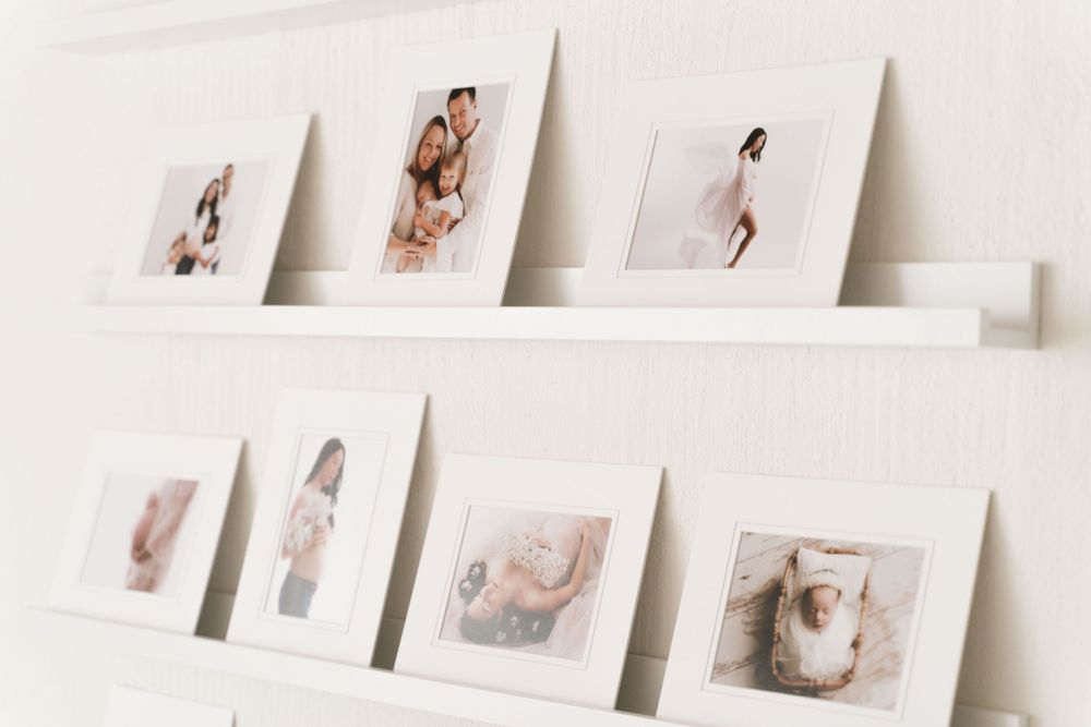 White wall-mounted picture ledges displaying framed newborn and maternity photography prints in a studio.