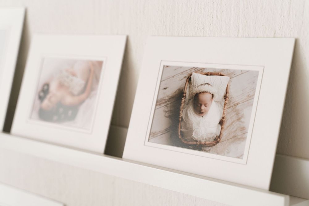 Close-up of framed newborn baby photos displayed on a white picture ledge shelf in a photography studio.