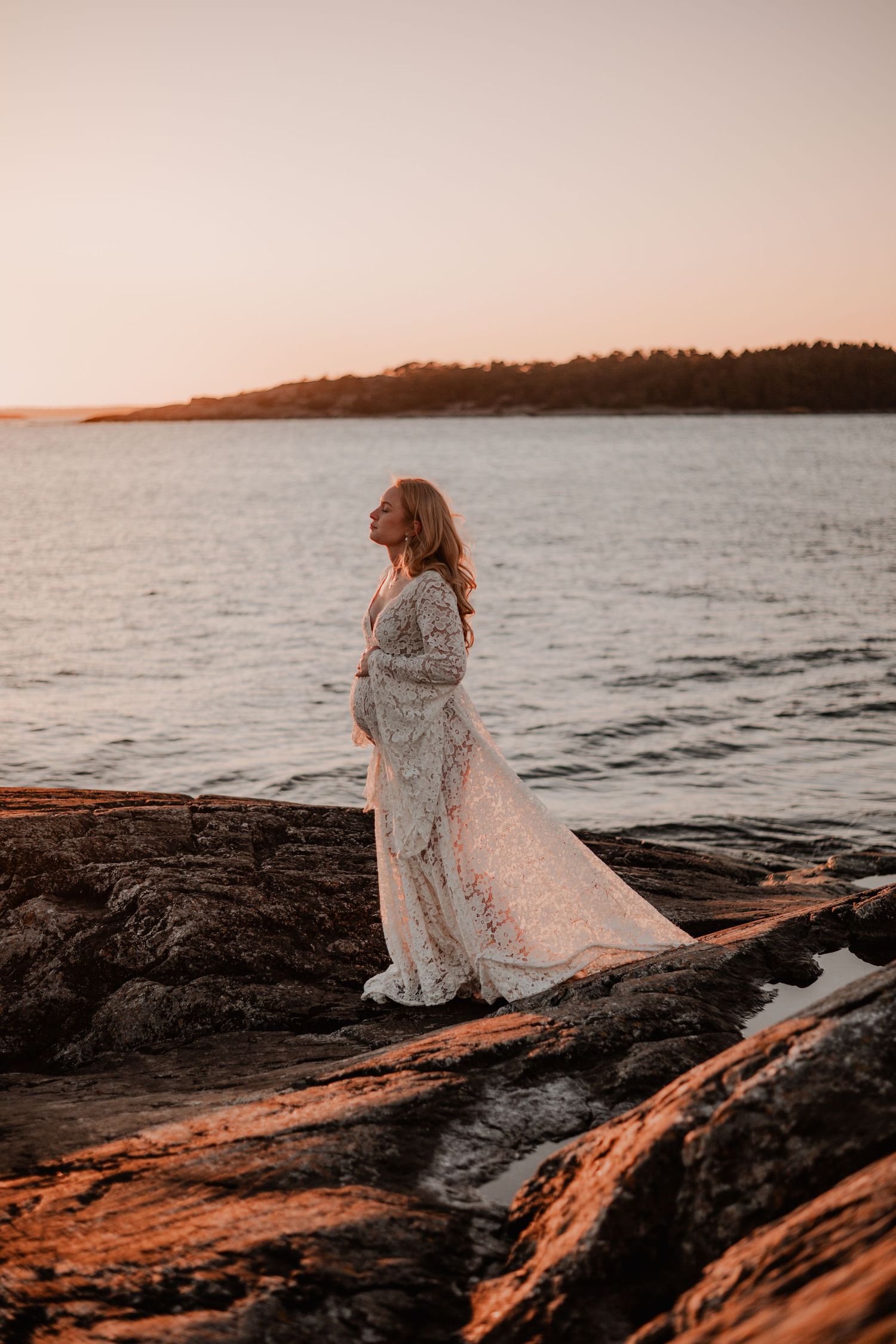 Gravidfotografering på en klippa i Nynäshamn i solnedgången i en bohemisk gravidklänning