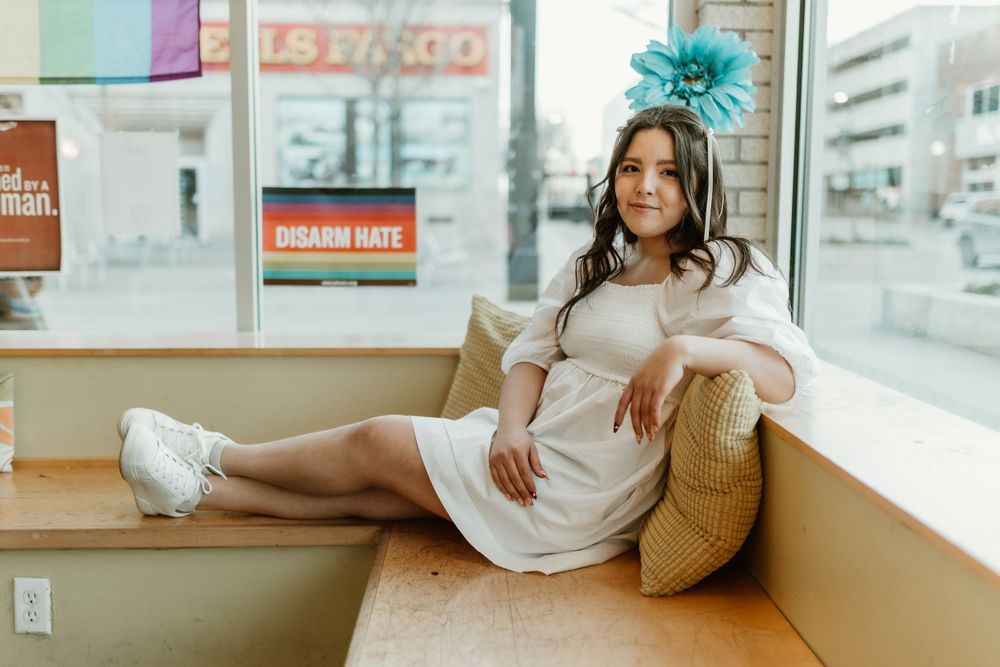 Person lounges on window bench in white dress and blue hair accessory.
