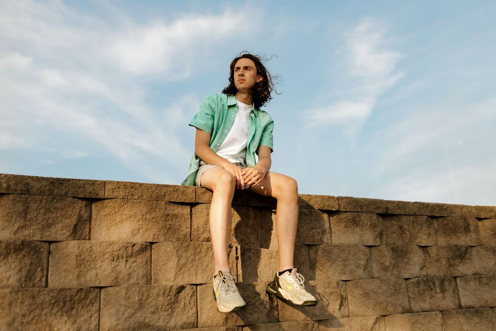 Person in casual attire sits on stone wall against blue sky.