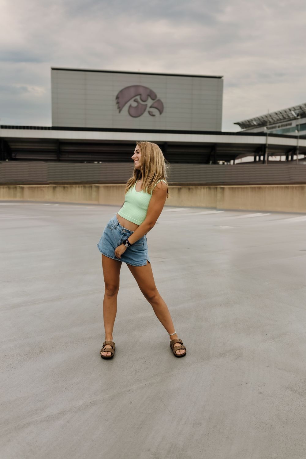 Casual summer outfit pose in front of Iowa Hawkeyes stadium logo.
