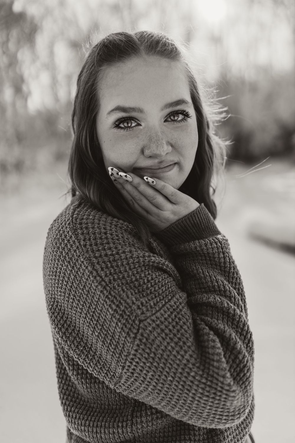 Black and white portrait of person in sweater with hand near face.