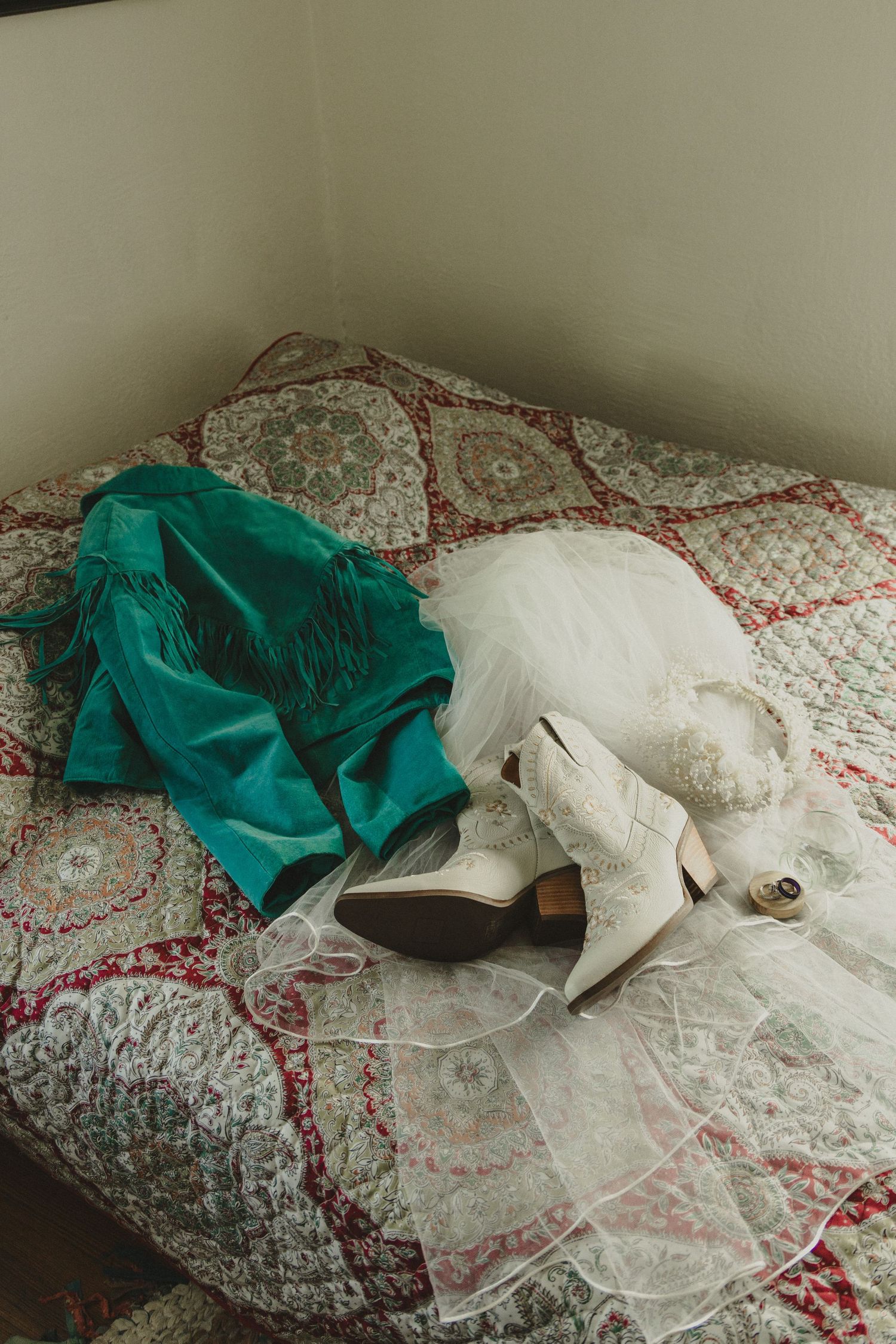 Wedding shoes and emerald green dress laid out on patterned bedspread.