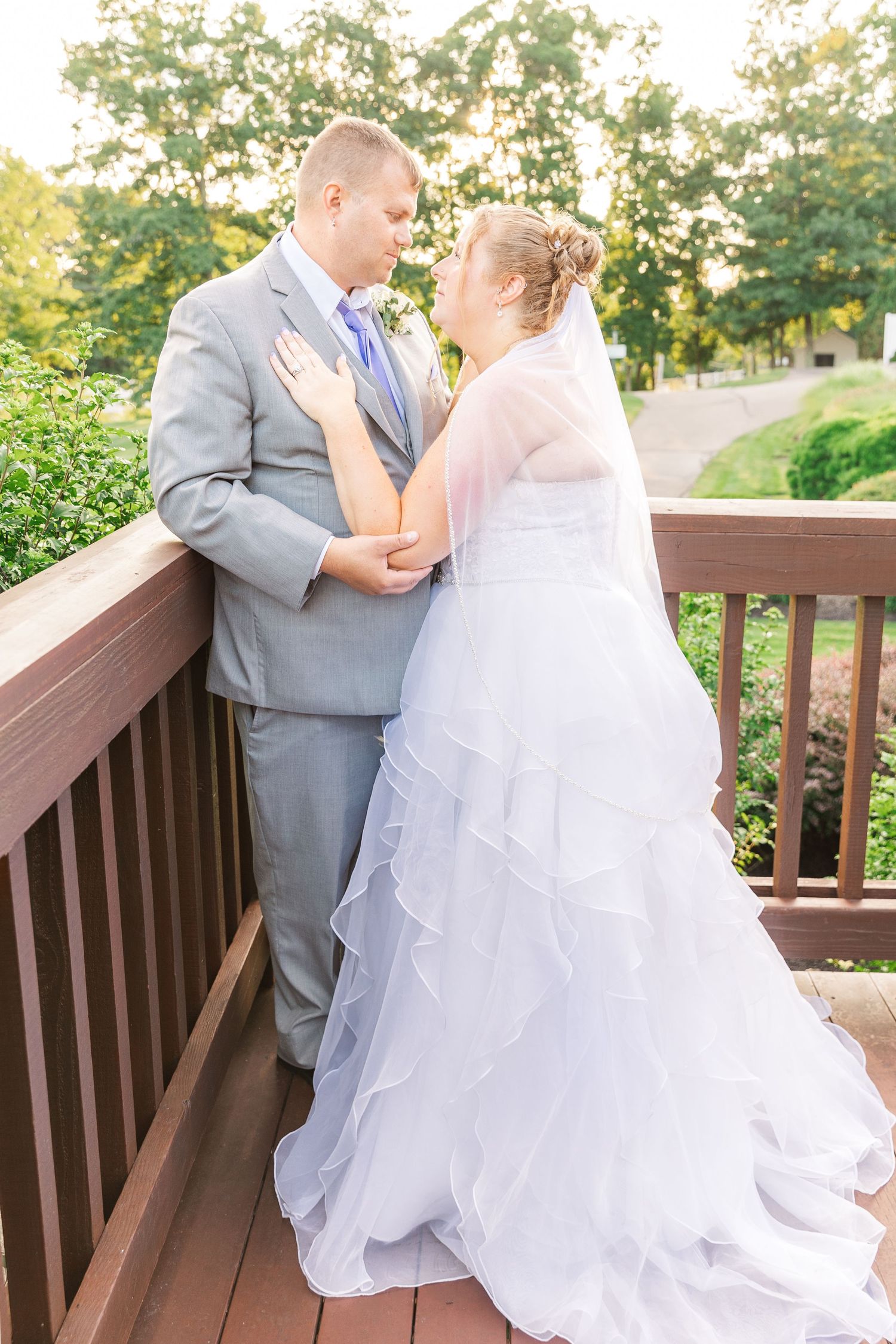 Couple embracing on wooden deck in formal wedding attire.