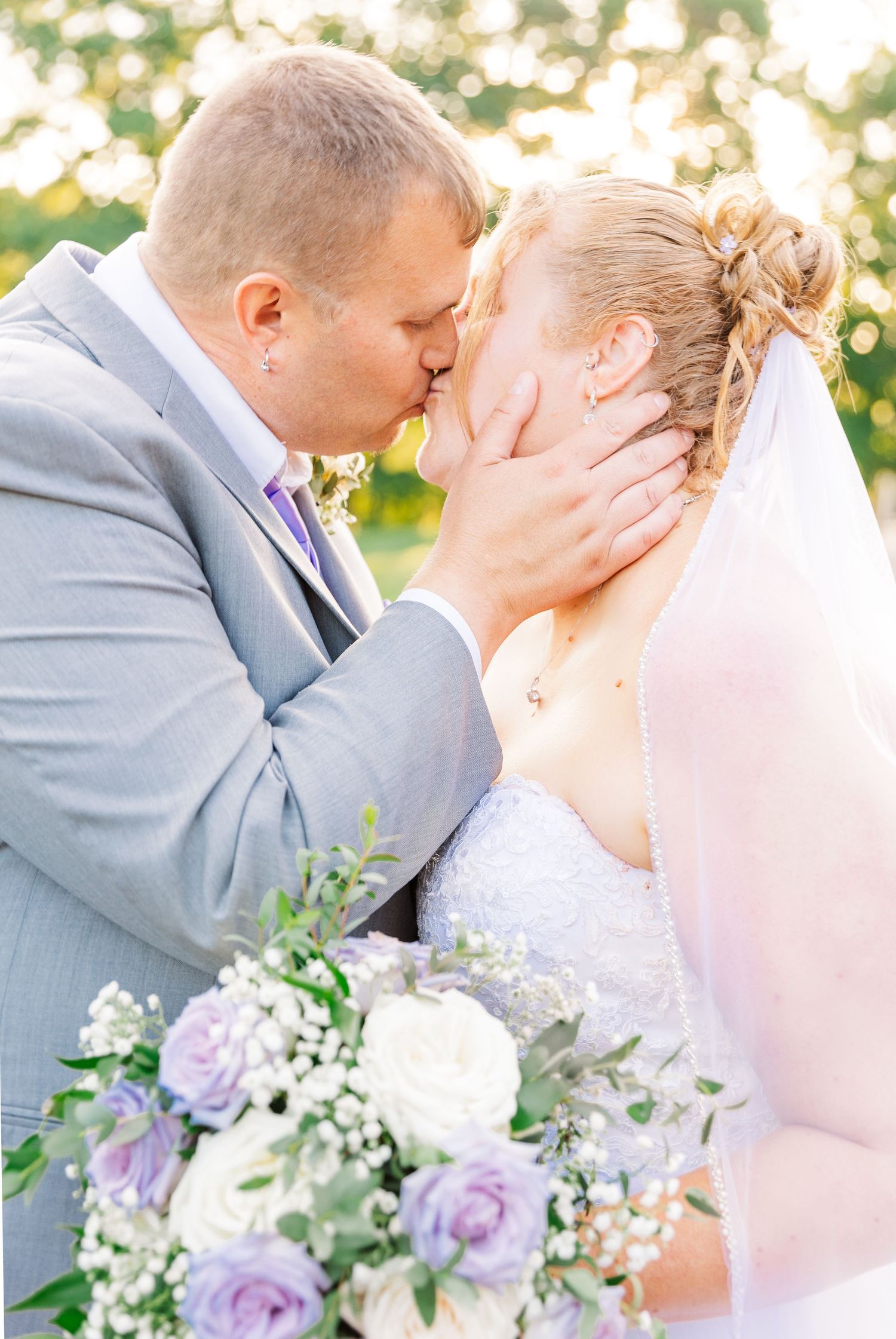Romantic kiss captured with purple and white bouquet in foreground.