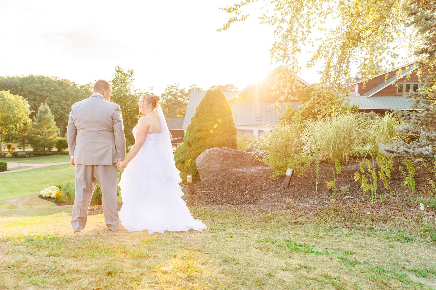 Newlyweds walking through garden landscape at golden hour.