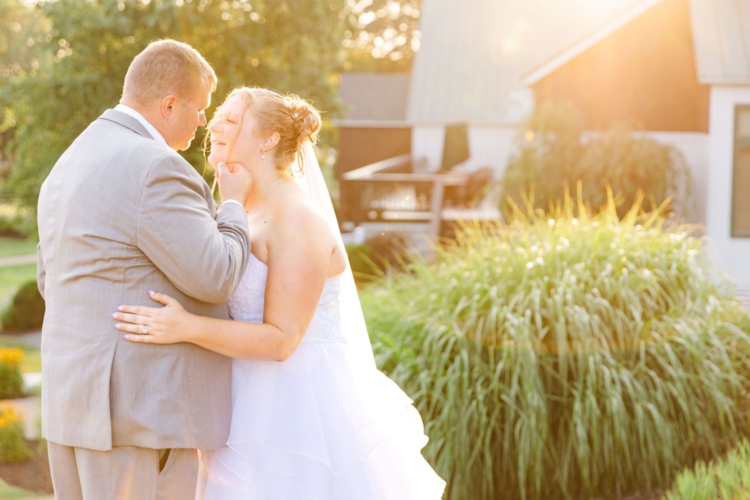 Couple embracing during sunset with ornamental grasses in background.