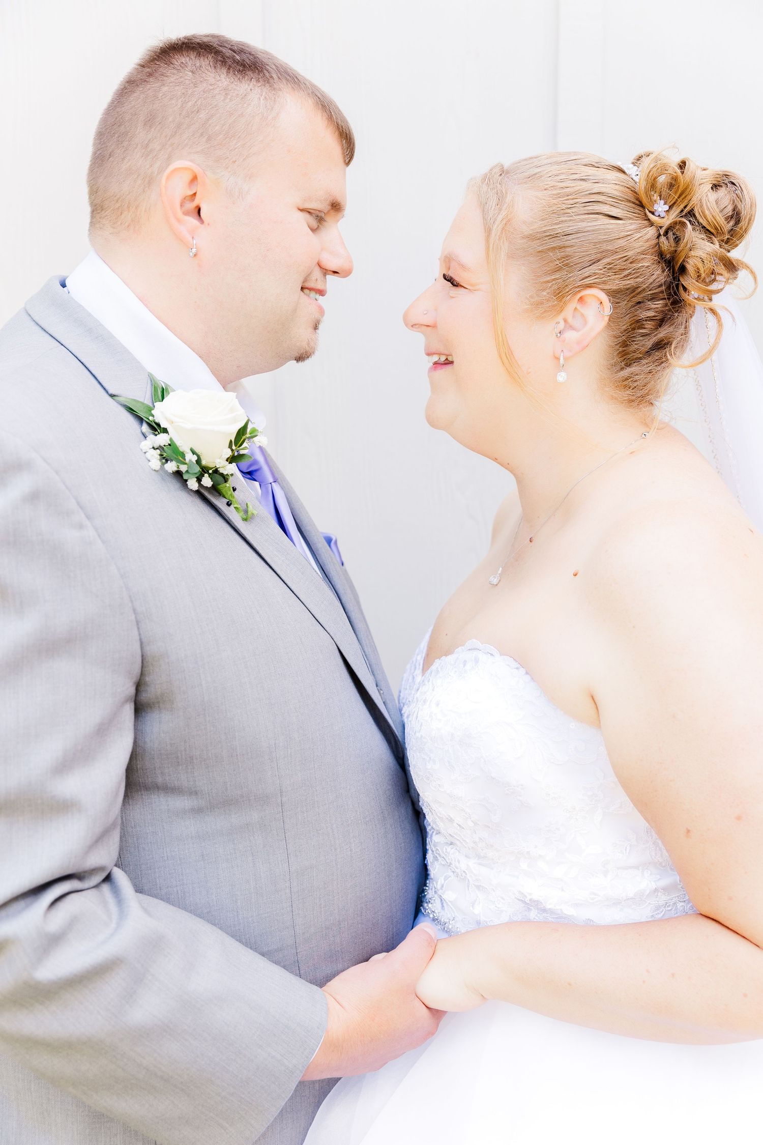 A tender moment between newlyweds in formal wedding attire against a white background.