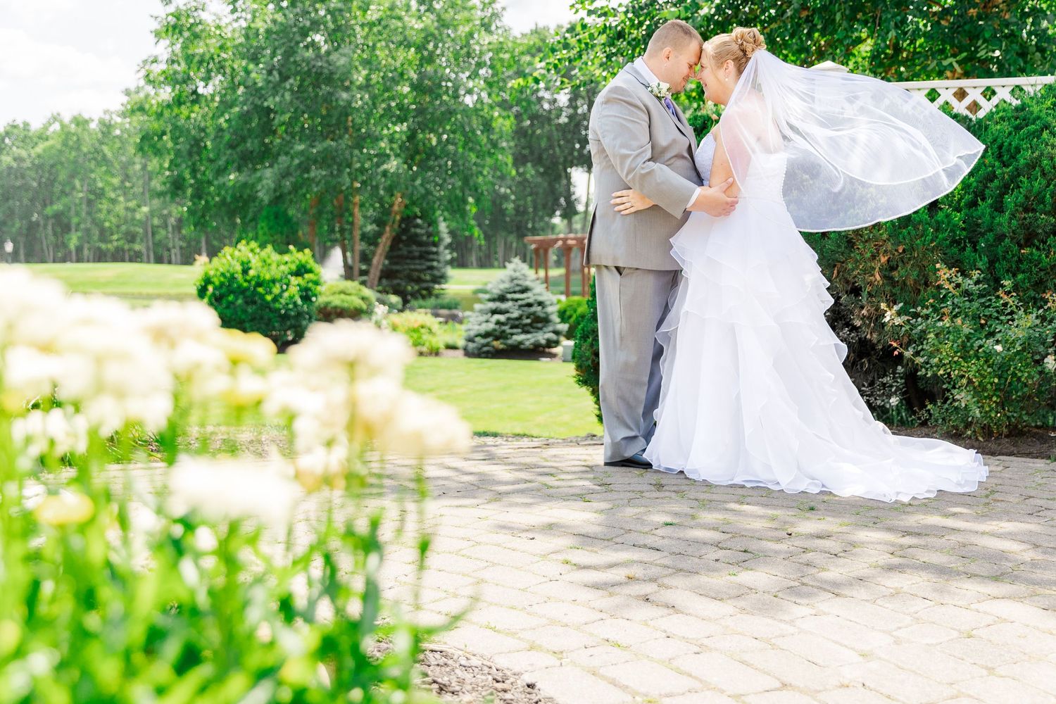 A romantic wedding moment captured on a stone pathway surrounded by summer garden landscape.