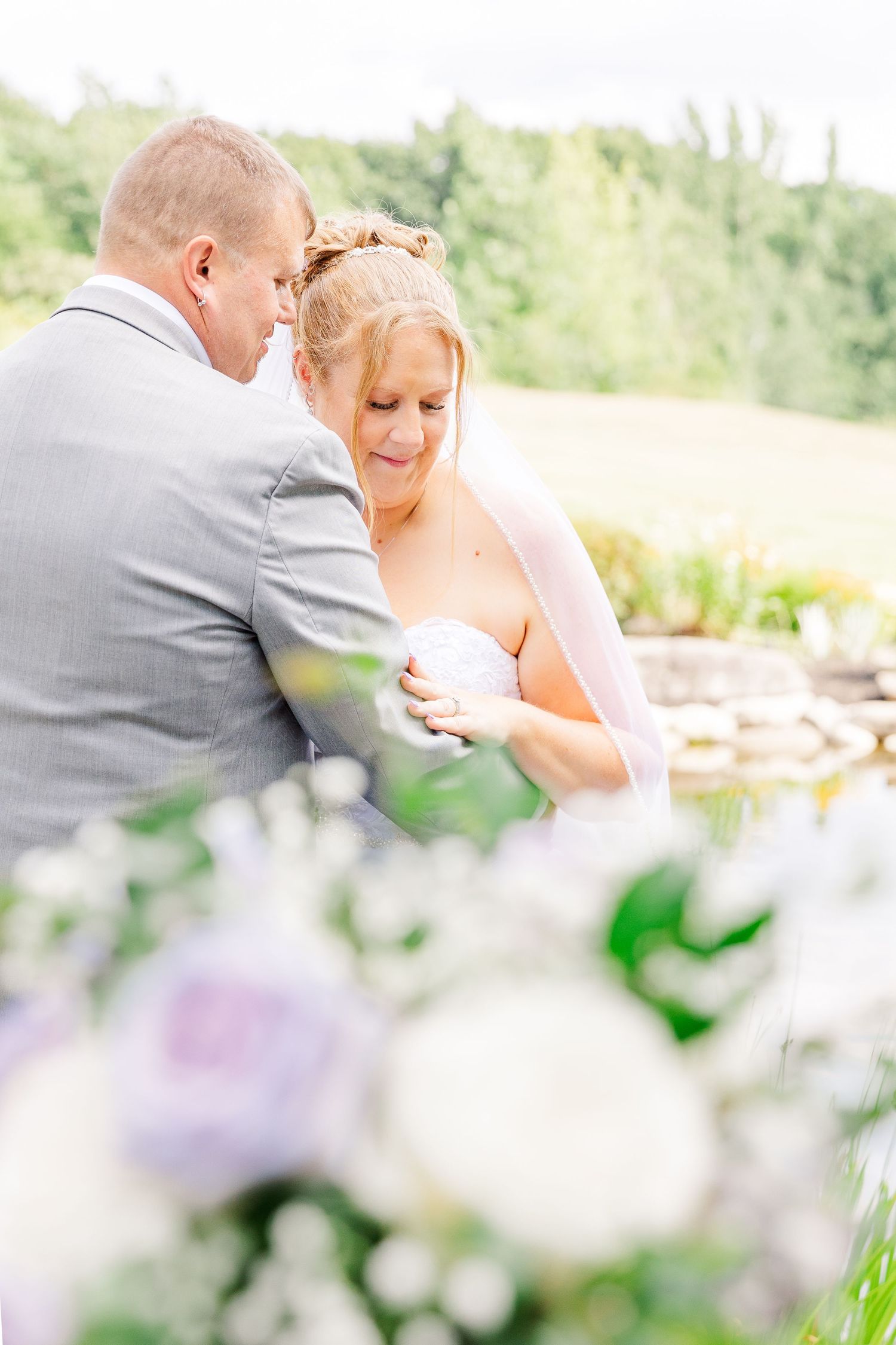 Couple shares tender moment together surrounded by purple and white flowers in garden setting.
