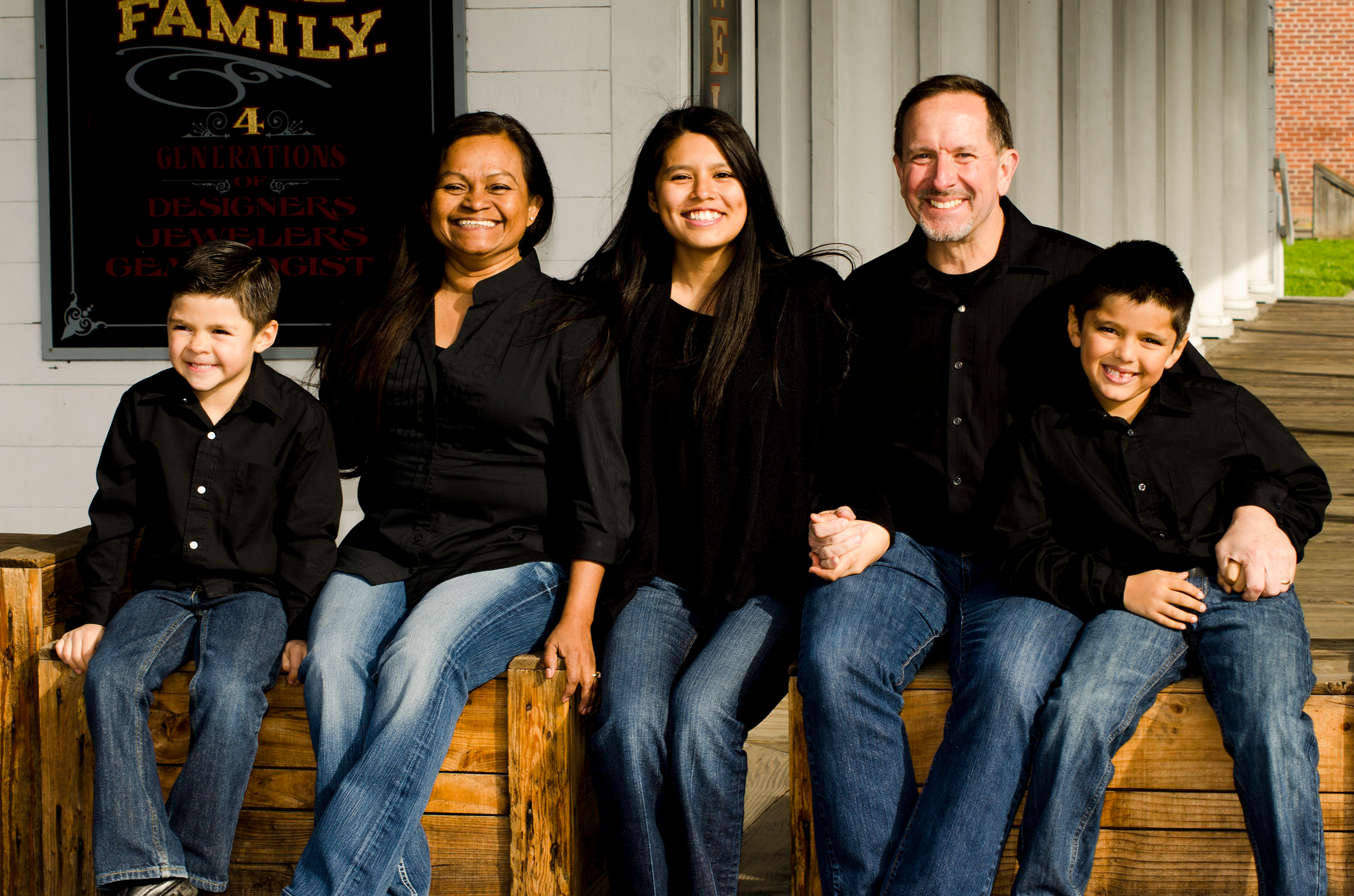 Large family group poses together on wooden steps wearing coordinated blue jeans and casual attire.