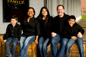 Large family group poses together on wooden steps wearing coordinated blue jeans and casual attire.